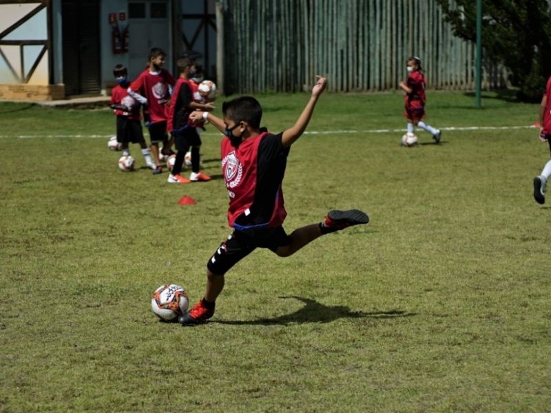 Crianças jogando futebol em campo gramado.